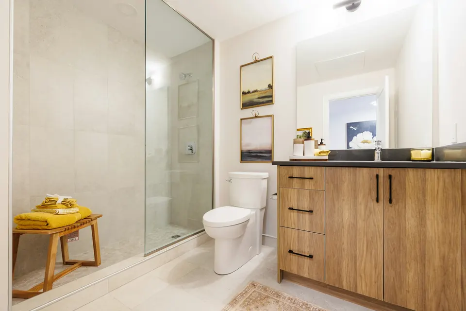 A bright bathroom with a wood vanity, white sink and glass shower