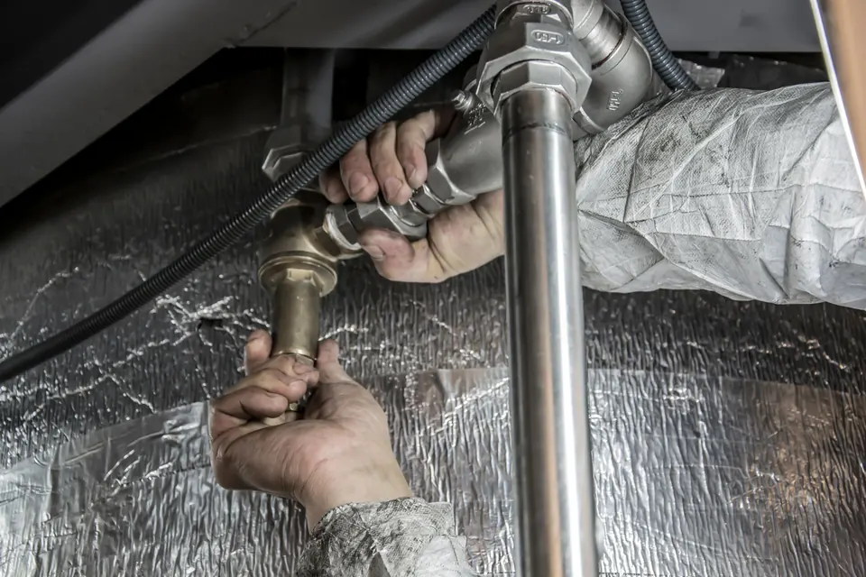 A plumber's hands tightening a brass fitting on a water line