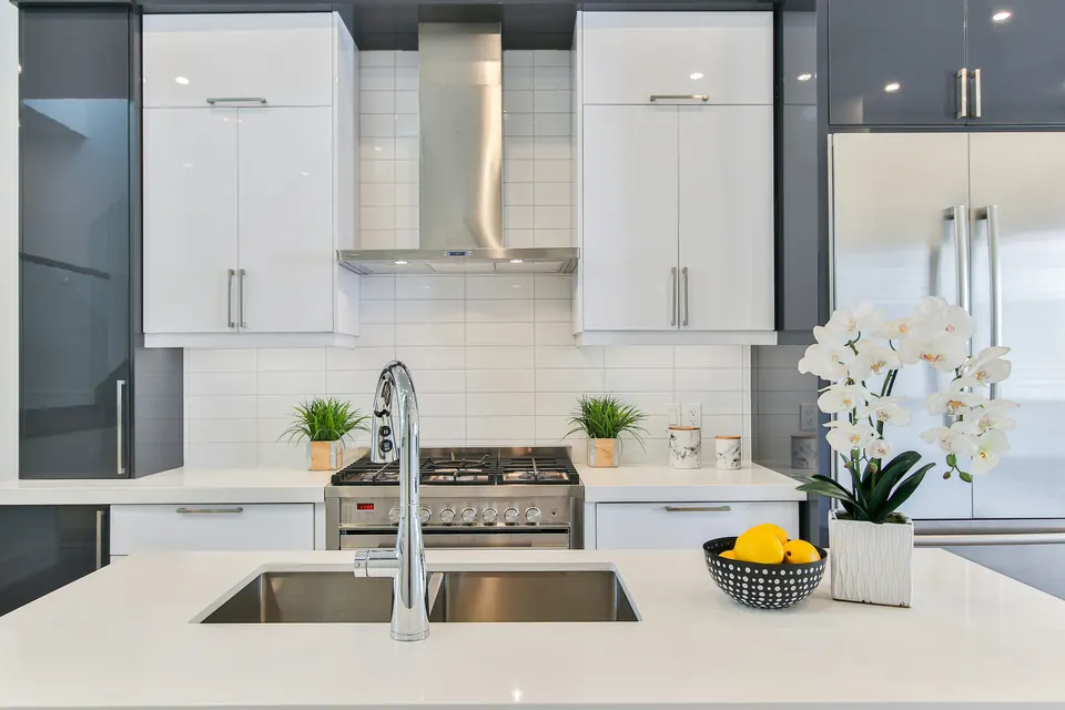 A modern white kitchen with a stainless sink and faucet on the island