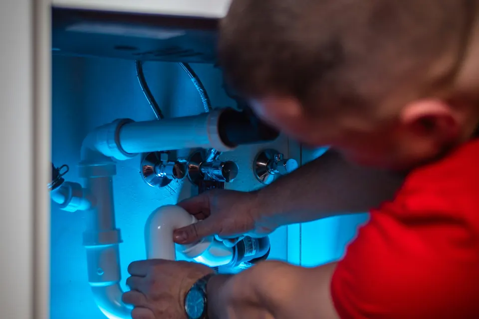 A plumber reaching under a sink cabinet to loosen a drain trap
