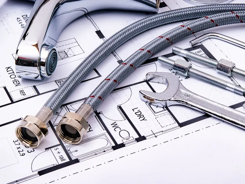 A new chrome faucet, braided supply lines and a wrench laid out on a floor plan
